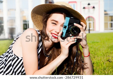 Outdoor fashion portrait of stylish photographer girl holding vintage camera,wear bright summer outfit,trendy straw hat,and look at camera.summer fall collection perfect in park sun shine body shape