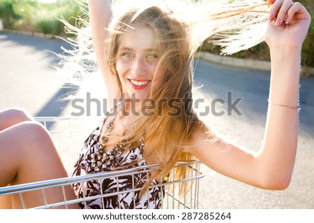 Happy screaming and laughing blonde girl sitting at shopping trolley and having fun. Pin up retro style.