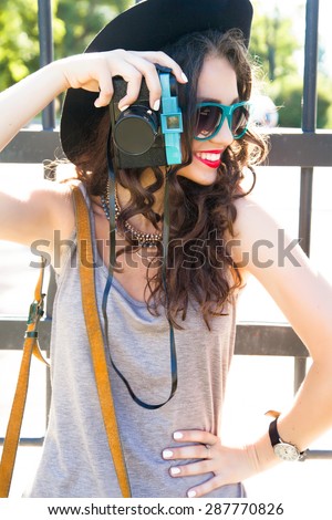 Close-up stylish portrait of young girl make picture and  posing on the street on stylish outfit,wear summer glamour sunglasses,summer light long dress,small bag and big  black hat.Look at camera