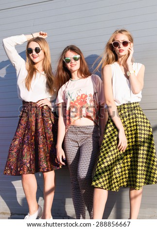 Young three happy beautiful girls best friends with perfect long tanned legs having fun at summer time,posing at park near wall,sending air kiss smiling and fun, joy,vacation time.Retro, vintage style