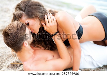 Two lovers at beach holding each other with lens flare and warm image tone,pretty girl cuddling with boyfriend on sand,shallow depth of field,loving happy couple on tropical beach,passion kiss