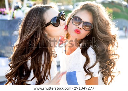 Outdoor lifestyle portrait of two best friends hipster girls wearing stylish bright outfits,  denim shorts and glasses, going crazy and having great time together.Laughing and send kiss,lovely friends