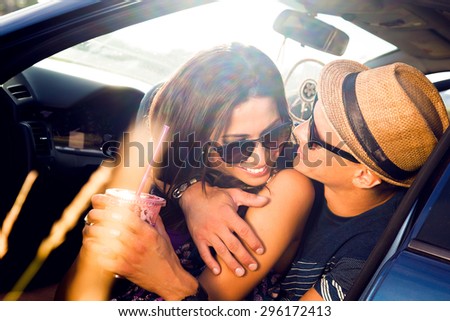 Young couple on road trip.Young couple sitting on the hood of their car with man answering a phone call and woman sitting by.Car is parked alongside coastal seashore with bright sunlight.sunset,bright