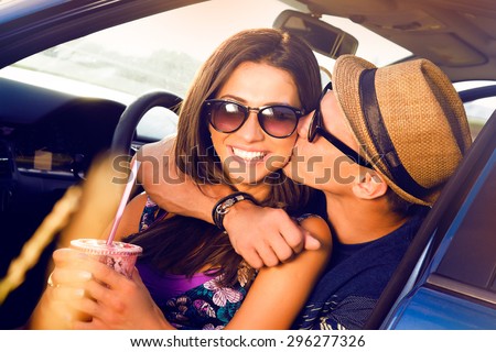 Laughing Romantic teenage hikers couple sitting on the hood of their car while out on a road trip.woman kissing boyfriend,smiling,outdoors.teen,purse,hat,Couple having fun on road trip on a summer day