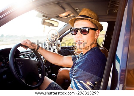 Happy young man going on holidays with friends,in a open top car.Loving couple enjoying on a road trip.Handsome man driving car on road,opposite the sunset,muscular man,hat,sunglasses,vintage style