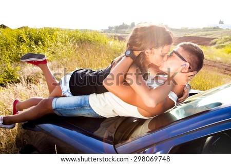 Sunshine Outdoor portrait of two happy teens,sensual couple laying on the car and kissing,enjoy their trip together to Europe,Trip to California,bright toned colors,sunset day,fitness couple,joyful