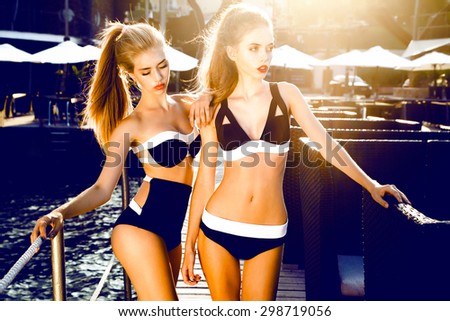 Close up lifestyle summer portrait of girls friends relaxed and getting sunbathe on the beach opposite the sunset,wearing bright bikinis,stylish and vintage.Swing tongue,relaxing,lounge zone,friends