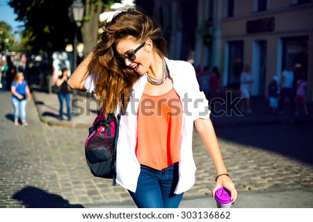 Summer sunny lifestyle fashion portrait of young stylish hipster woman walking on street,wearing cute trendy outfit,drinking hot latte,smiling enjoy weekends,travel with backpack,coffee,rest,lounge