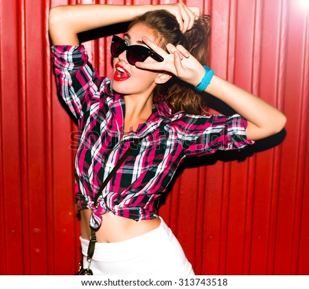 Fashion studio portrait of pretty young hipster blonde woman with bright sexy make up and glasses , wearing stylish urban t shirt and hat, White urban wall background.Trendy image of a dark head woman