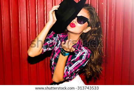 Funny stylish sexy smiling beautiful young hippie woman model in summer white fresh hipster clothes sitting in the street,bright colored clothes,street fashion,send kiss,red lips,black hat and glasses
