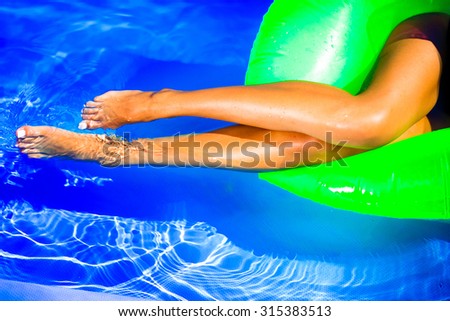 Young pretty fashion woman body posing in summer in pool with clear water lying on mattress in black bikini and having fun.long legs,relaxing time,chilling time,holidays,pool party,wet body,laying