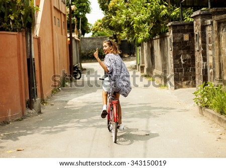 Healthy and happy cyclist woman riding fast a bicycle in a park.cute amazing smiling girl,floral dress summer vintage style,street evening sunlight.fashionable sunglasses,trendy street style.Bali boho