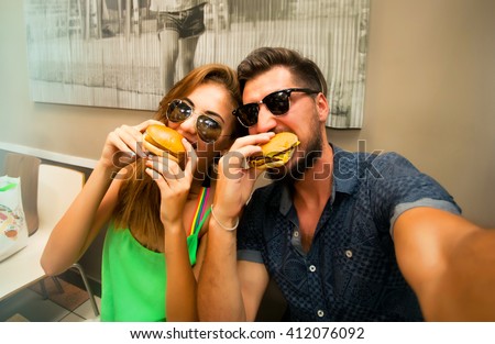 Happy lovers,attractive woman and man traveling in tropical island enjoying romance. Attractive couple making selfie,smiling and have fun together.Couple Eating big burgers,cheeseburger and coke.fun
