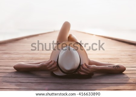 close-up young slim woman laying on pier, Mediterranean Sea,azure water,sunny,tanned skin,listening music,headphones,black swimsuit,sexy body, sunbathing, tropical vacation, relaxed,music,laying