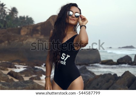 Pretty fashion sport style woman smiling and relaxing in the ocean in summer.wet long hair,treatment,print swimsuit,Outdoor portrait of cute girl in sunglasses in tropic island