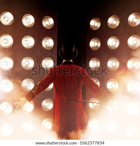 Showman. Young male entertainer, presenter or actor on stage. Back, arms to sides, smoke on background of spotlight