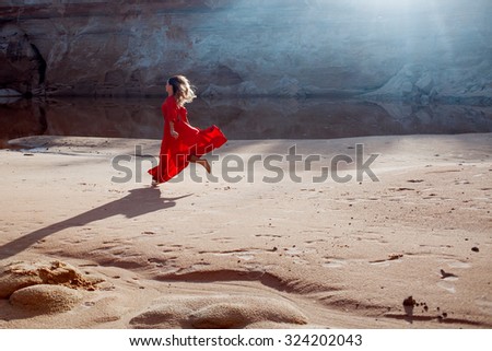 Woman in red waving dress with flying fabric runs on the background of sands career