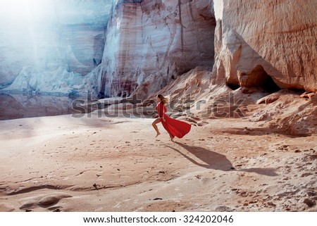 Woman in red waving dress with flying fabric runs on the background of sands career