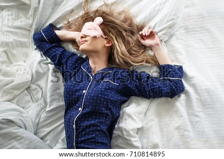 Cute blonde in her bed in blue pajamas and sleep mask, top view