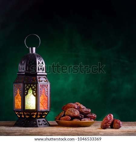 Ramadan concept. Dates close-up in the foreground. Ramadan Lantern on a wooden table. Textured green wall background. Space for text on the right. Square 1:1 frame.