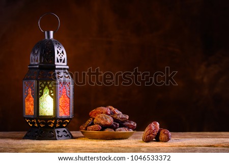 Ramadan concept. Dates close-up in the foreground. Ramadan Lantern on a wooden table. Textured yellow wall background. Space for text on the right.