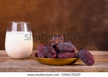 Holy month of Ramadan concept. Righteous Muslim Lifestyle. Fasting. Dates and glass of milk. A plate with dates on a wooden table. Place for text. Dark browen background.