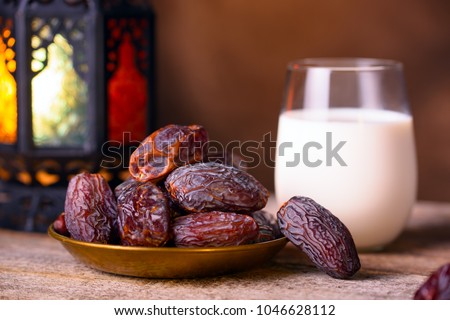 Ramadan concept. Dates close-up in the foreground. Ramadan Lantern and glass of milk on a wooden table. Dark brown wall background. Selective focus, low depth of field, bokeh