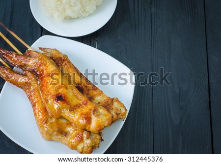 Grilled chicken wings and sticky rice in dish  on wooden background selective focus on dark tone