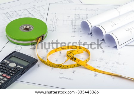 Tape measure and calculator placed on the desk, filled with building plans. In order to work in a building