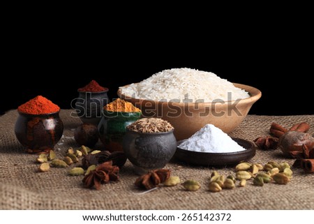 Rice, spice powders and seeds on the table covered with burlap cloth. Black background