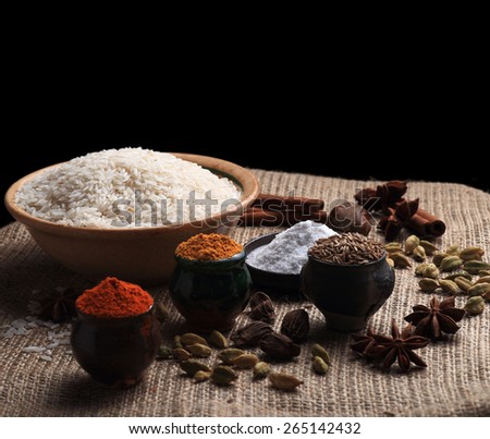 Rice, spice powders and seeds on the table covered with burlap cloth. Black background