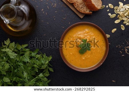 Pumpkin and carrot soup, bread and green on dark background. Top view
