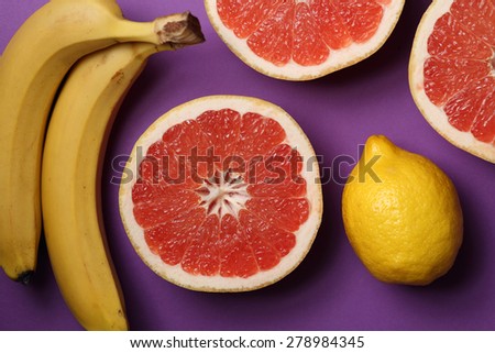 Lemon, grapefruits and bananas on bright lilac background