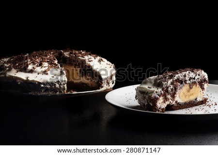 Piece of banana and chocolate cake on white porcelain plate. Dark background