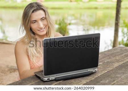 Female with a laptop sitting in a wood table by the lake /Female with laptop/ Women working, sitting in a wood table by the lake. Girl Studying outside.