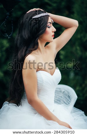 beautiful girl the bride sits on a chair. Portrait of the brunette with long hair and beautiful makeup