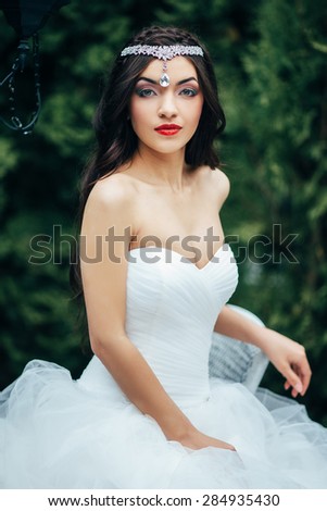 The girl brunette with long hair with a beautiful makeup and hairstyle. The bride sits on a chair in a green garden