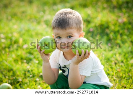 Happy little boy laughs and walks outdoors and holding big green apples. Child biting and eating a large green apple in the garden.