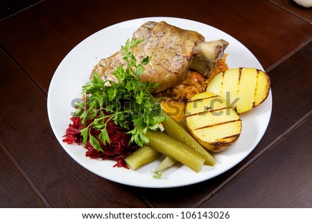 pork leg with greens, spices, potatoes and vegetables on white plate. turkey leg. chicken leg.