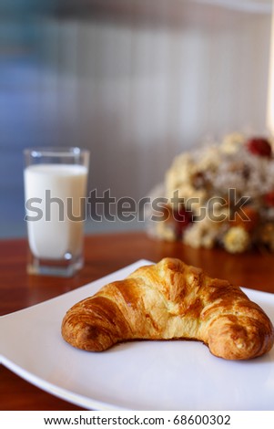 Appetizing croissant on a white plate and glass of milk