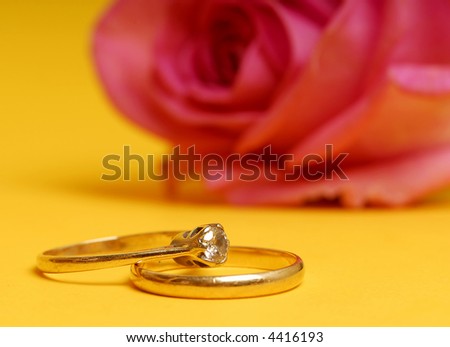 wedding and engagement ring on a yellow background with pink rose, summer wedding concept.