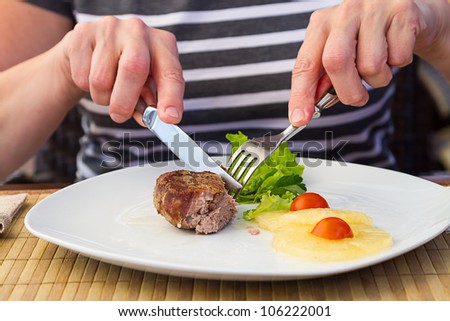 Woman cuts cooked medallion with a fork and knife in a restaurant