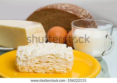 Cottage cheese on a yellow plate, cheese, eggs, milk mug and rye bread