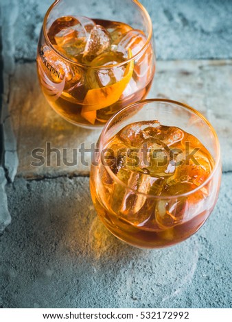 Two orange campari cocktails ( Old-Fashioned / Negroni / Aperol Spritz) with ice on a contrast turquoise background, vertical. Light through the liquid