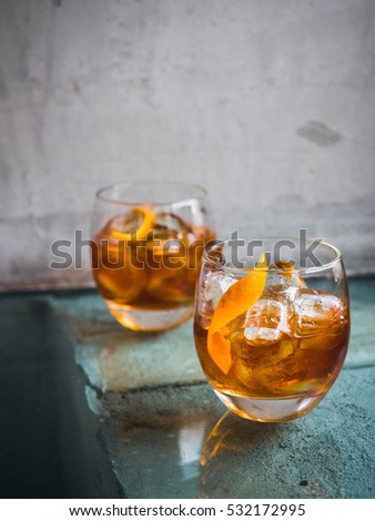 Two orange campari cocktails ( Old-Fashioned / Negroni / Aperol Spritz) with ice on a contrast turquoise background, vertical. Light through the liquid