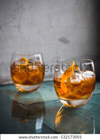 Two orange campari cocktails ( Old-Fashioned / Negroni / Aperol Spritz) with ice on a contrast turquoise background, vertical, side view. Light through the liquid