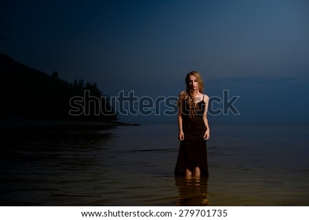 the beautiful young girl in a black dress with long hair costs in water, having hung the head
