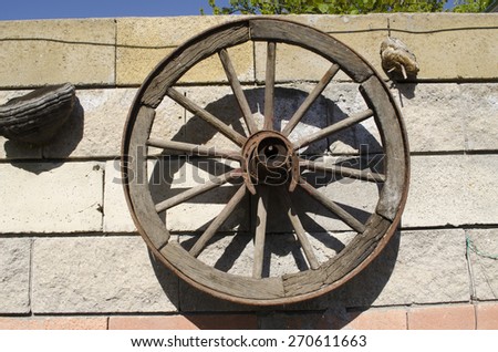 Old wooden wheel with rusty iron horseshoe hanging on a stone wall in the garden
