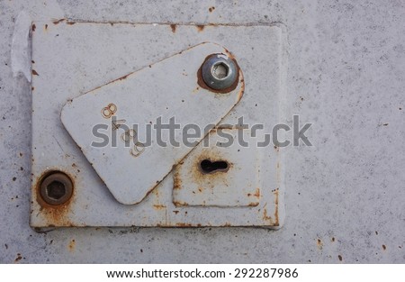 Heavy duty metal, steel lock, keyhole and cover plate on a steel security door, with an imprinted stamped number. Distressed and rusty.