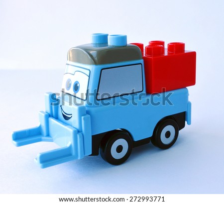 A blue smiling toy truck with a red squared constructor block on the white background